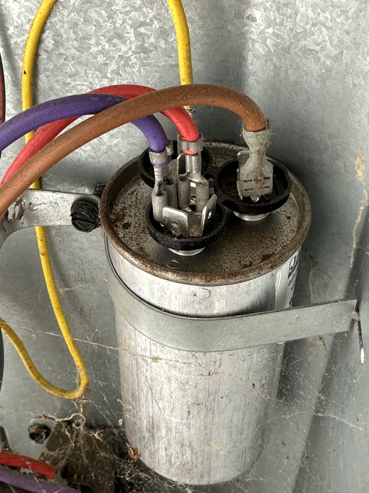 The old dual run capacitor mounted inside the condenser with wires attached to its terminals