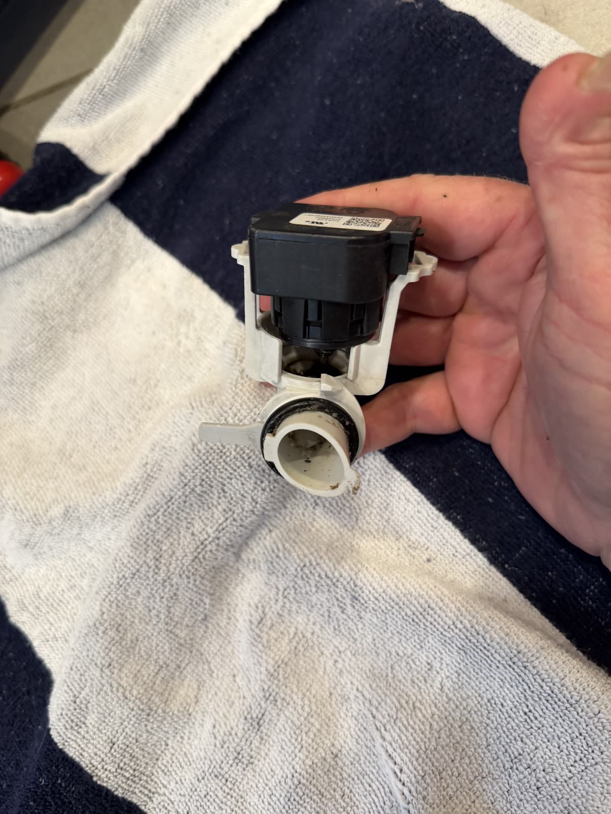 The old GE dishwasher pressure sensor held in hand after removal, with grime around the port
