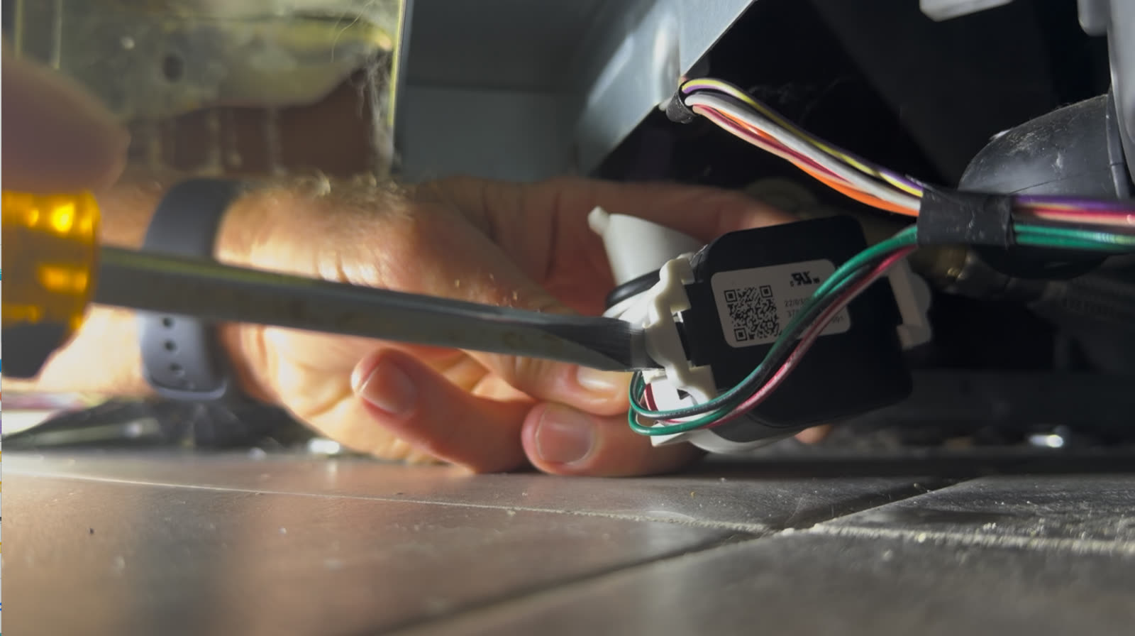 A small screwdriver releasing the wiring harness clip on the dishwasher pressure sensor