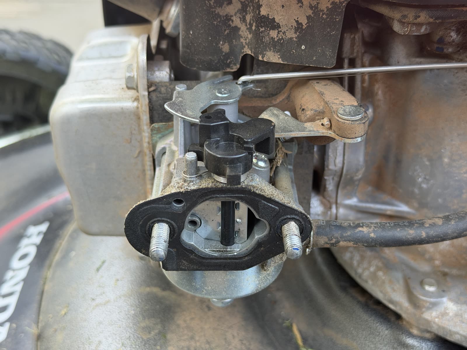 The new carburetor mounted on the engine studs with linkage and springs connected and the insulator gasket visible
