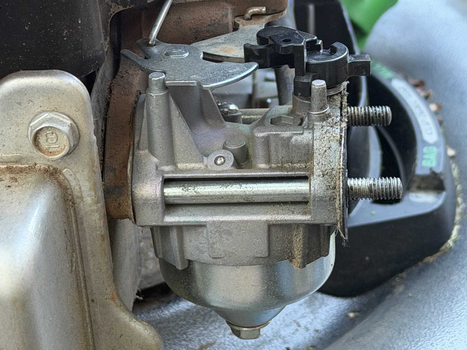 Side view of the new carburetor seated on the engine, float bowl visible, mounting studs protruding