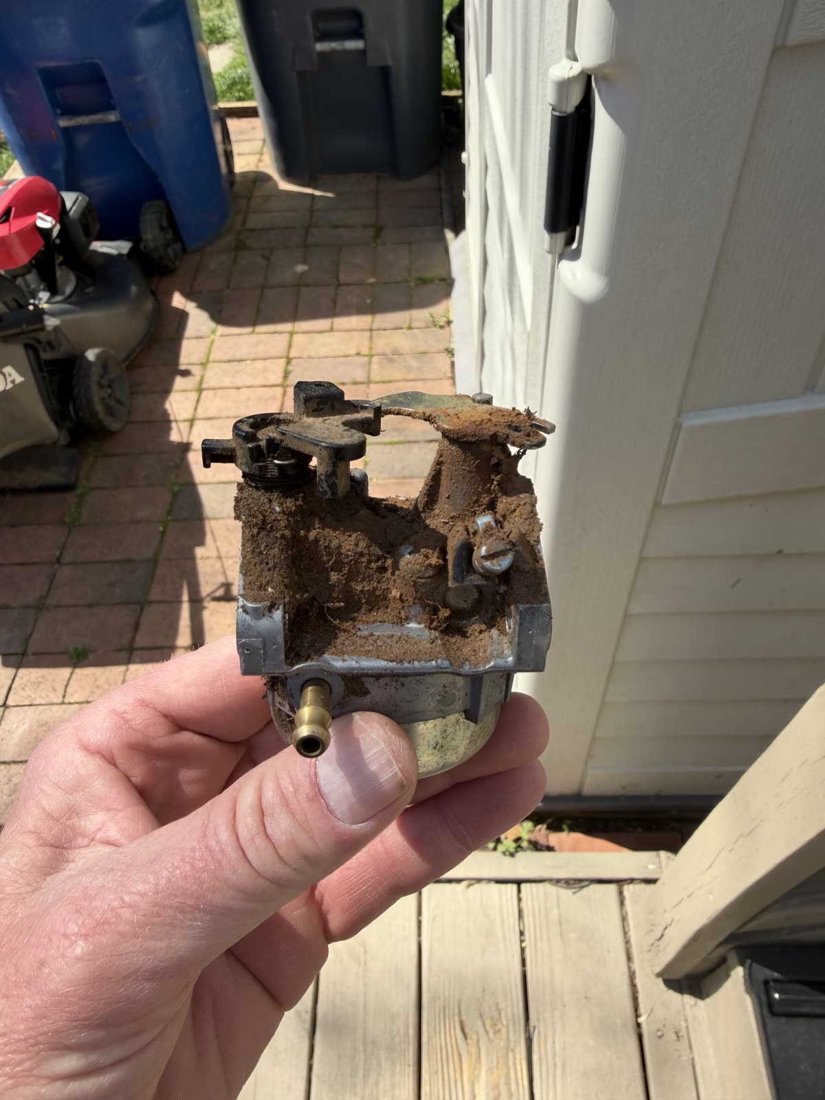 The old carburetor held in hand just after removal, caked in dirt and grime